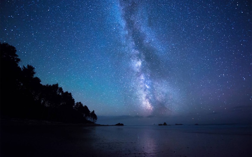 The Milky Way in a purple and blue starry night sky over a body of water