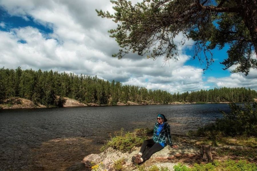 Person relaxing on a rocky shore under a blue sky with billowy clouds