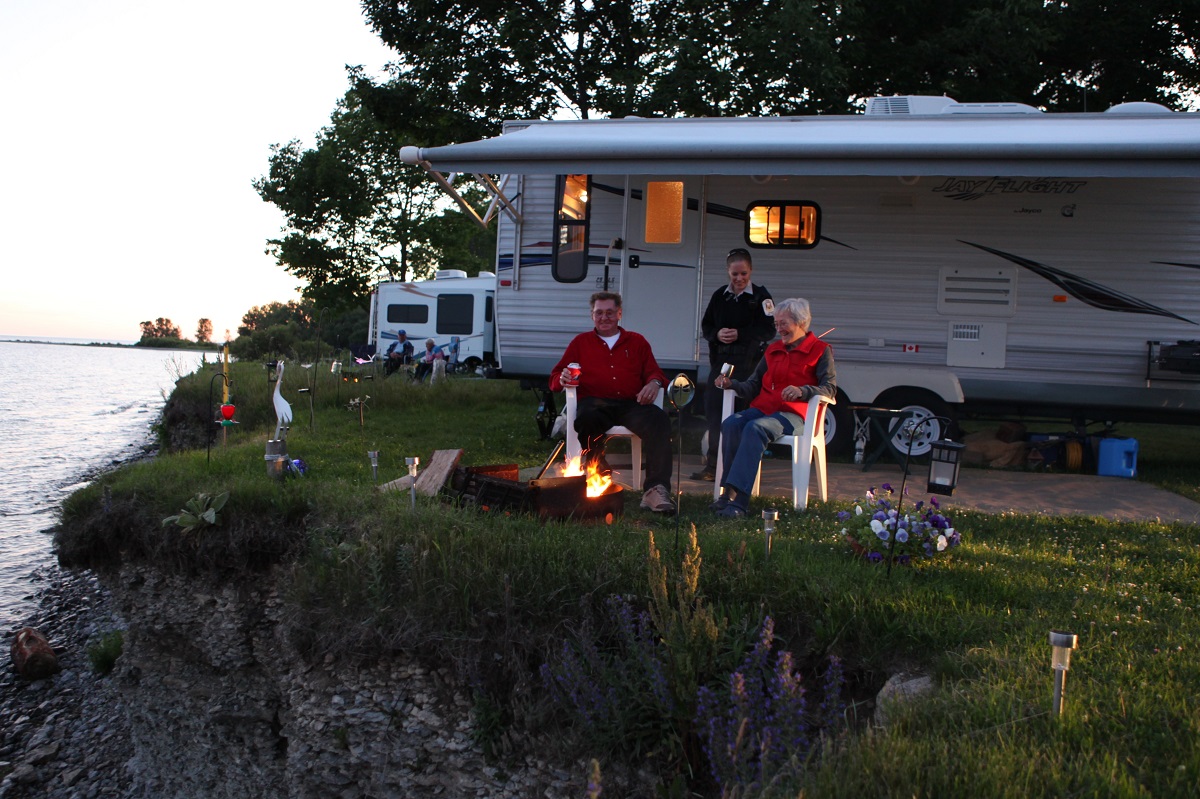 Couple sitting around their fire, next to RV parked on a waterfront campsite at Presqu'ile