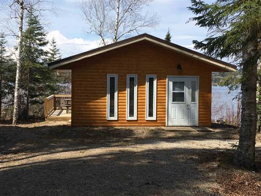 Wooden cabin with three long, narrow windows and white trim on the shore