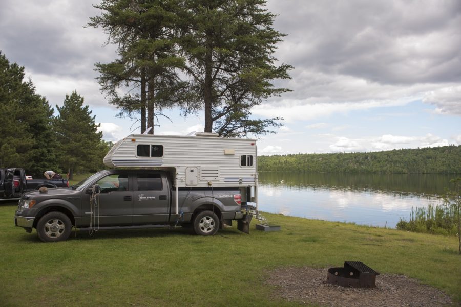 RV backed up to the shore of a lake on a grassy campsite right on the water