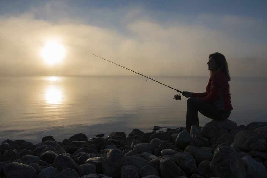 Silhouette of a woman fishing on a rocky shore