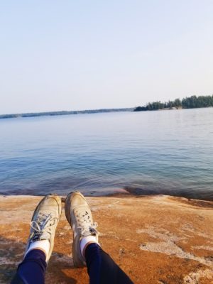 The feet (in sneakers) of someone on the beach looking towards the water