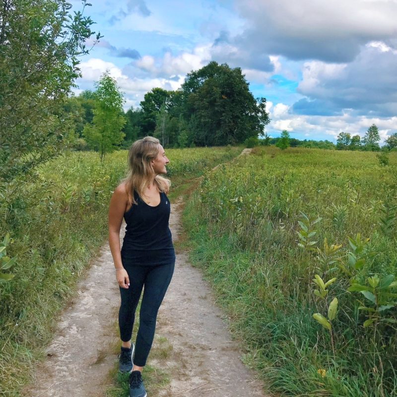 Lady in black active wear looking back in a field with a sky