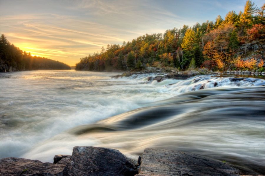 River with autumn forest in the background and sun setting in the sky