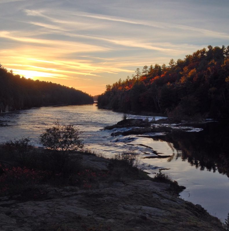 Sun setting over river with forest on all sides