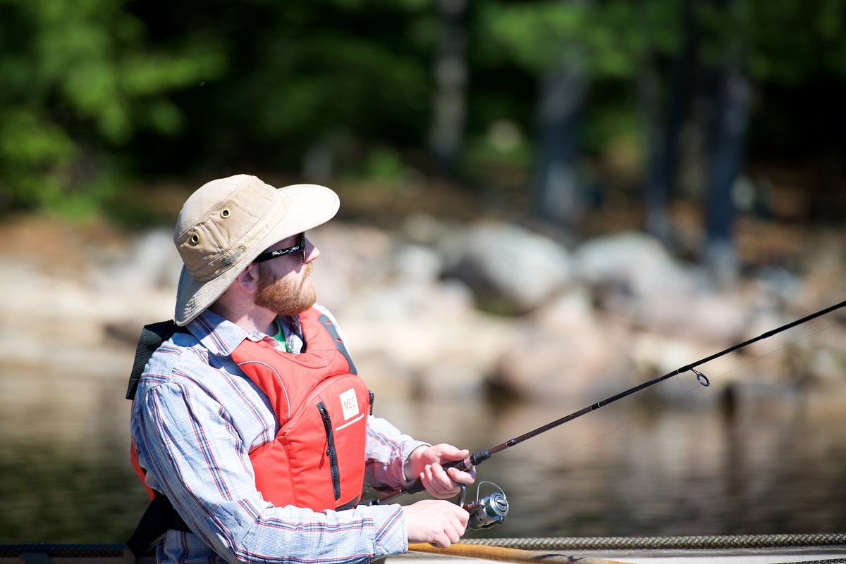 Guy with tilley hat and a life jacket in a boat, fishing