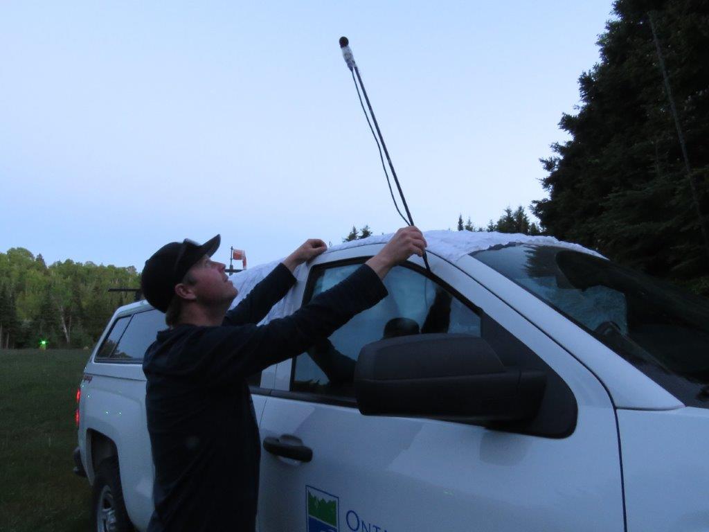 Guy putting an antennae on top of a truck at dusk