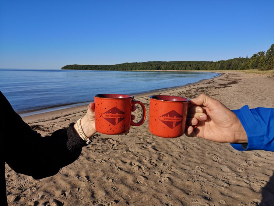 two people holding orange "ontario parks" mugs in front of beach