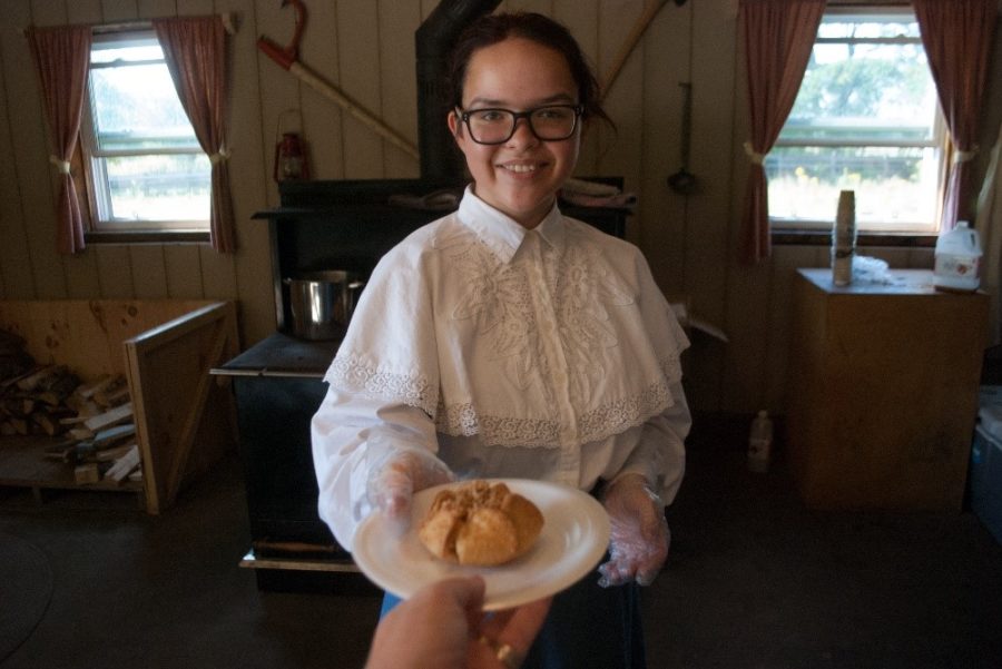 Woman in Victorian clothing is handed a plate with a pastry