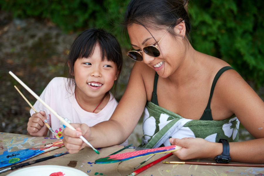 A mother and daughter painting miniature paddles at a picnic table. 