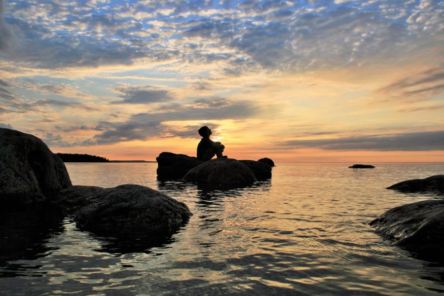 Silhouette of a boy sitting on a rock watching a sunset 