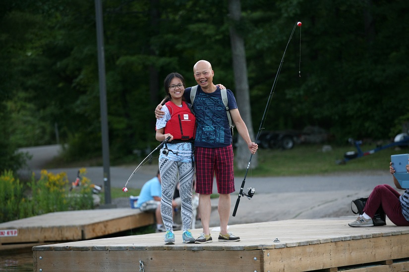 Man and daughter smile at camera with fishing rods on dock