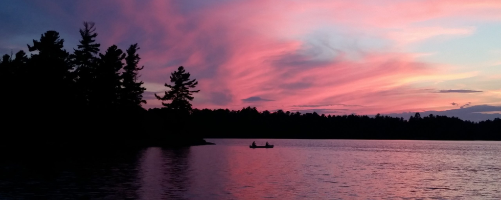 A pink sunset on a lake with a canoe in the distance