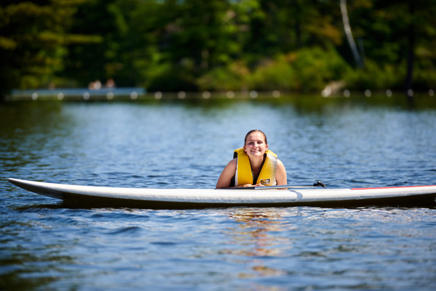 Stand up paddler in the water resting on board smiling