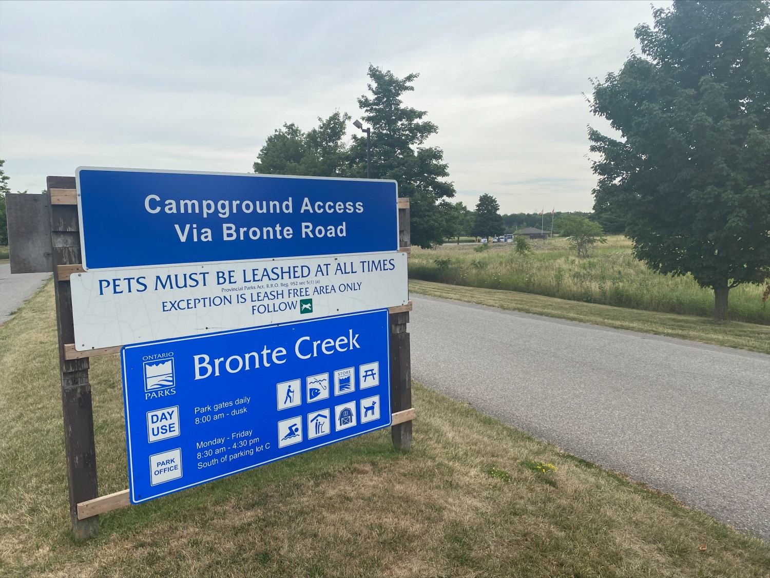 A blue and white Ontario Parks sign on the side of a road displaying visitor information for Bronte Creek Provincial Park