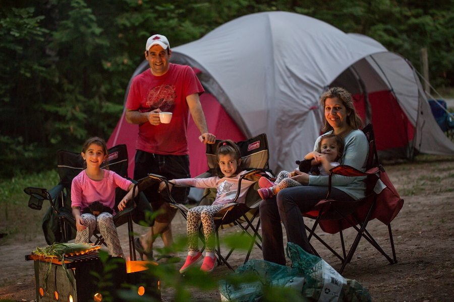 Family sits around campfire by tent