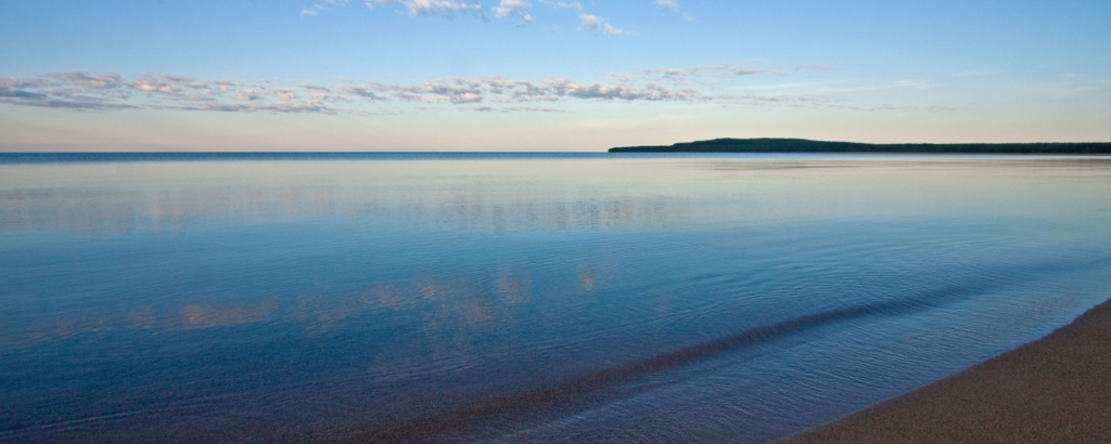 Still smooth lake reflecting the blue of the sky, along a beach