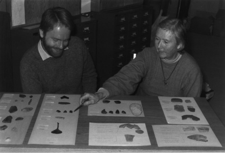 The two site in front of a table with several archaeological finds in front of them.