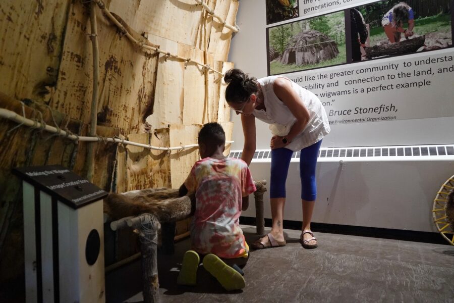 Visitors inside wigwam reading signs and listening to stories