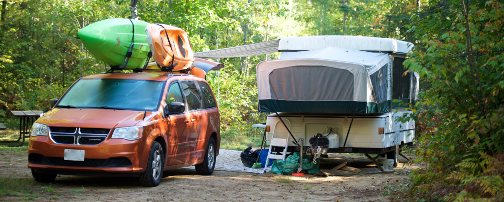 A trailer on a campsite with a vehicle with a kayak on top