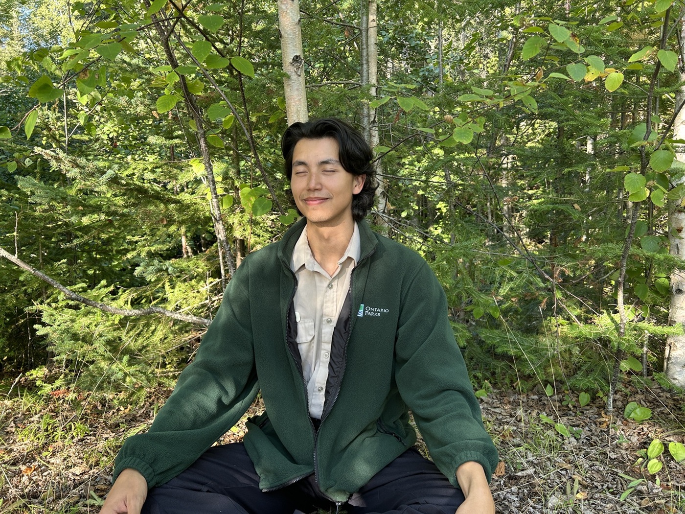 staff member sitting cross-legged in the forest with his eyes shut