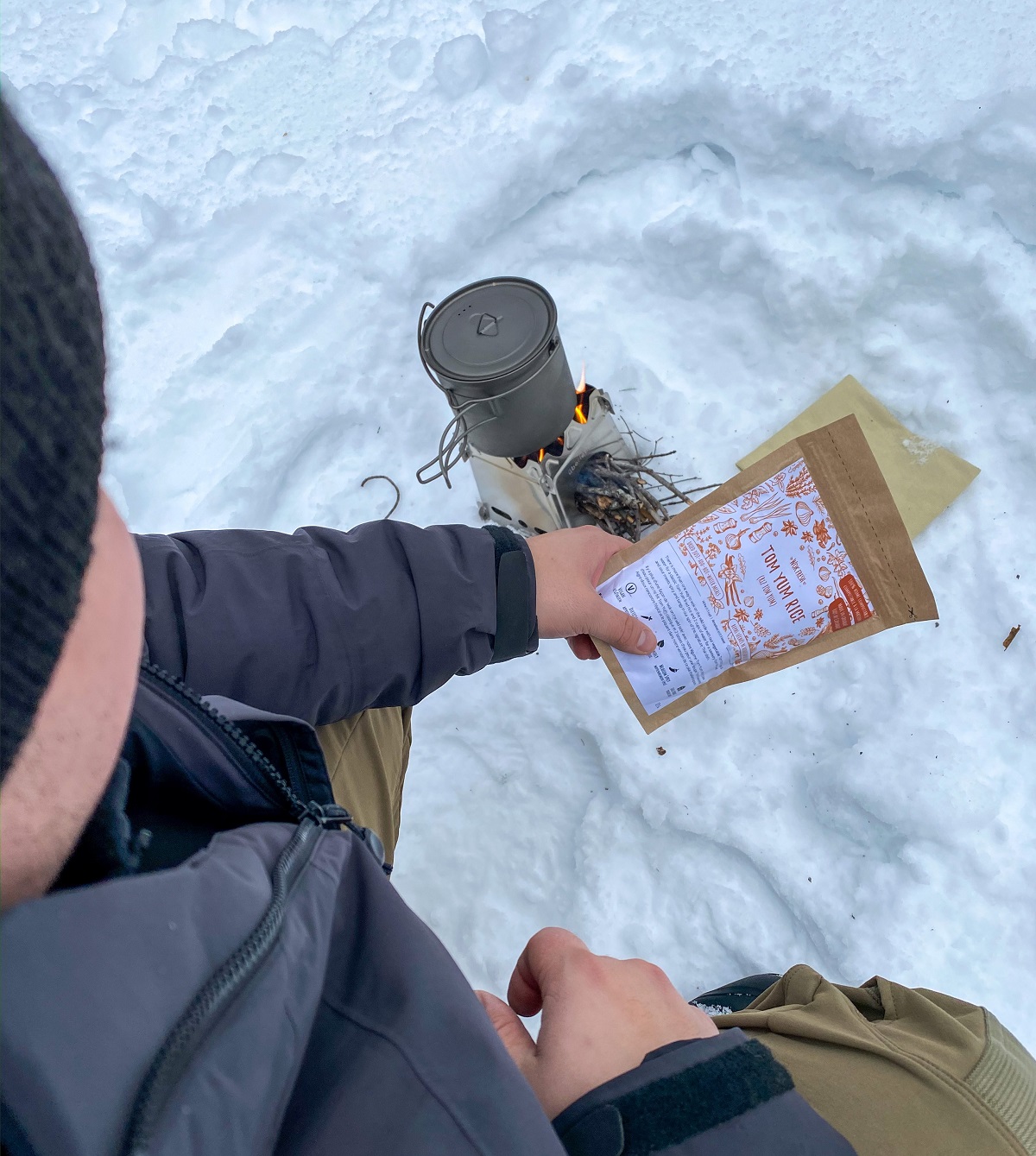 Man warming up food on a small stick fire in the winter