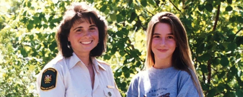Staff member and woman stand in front of tree