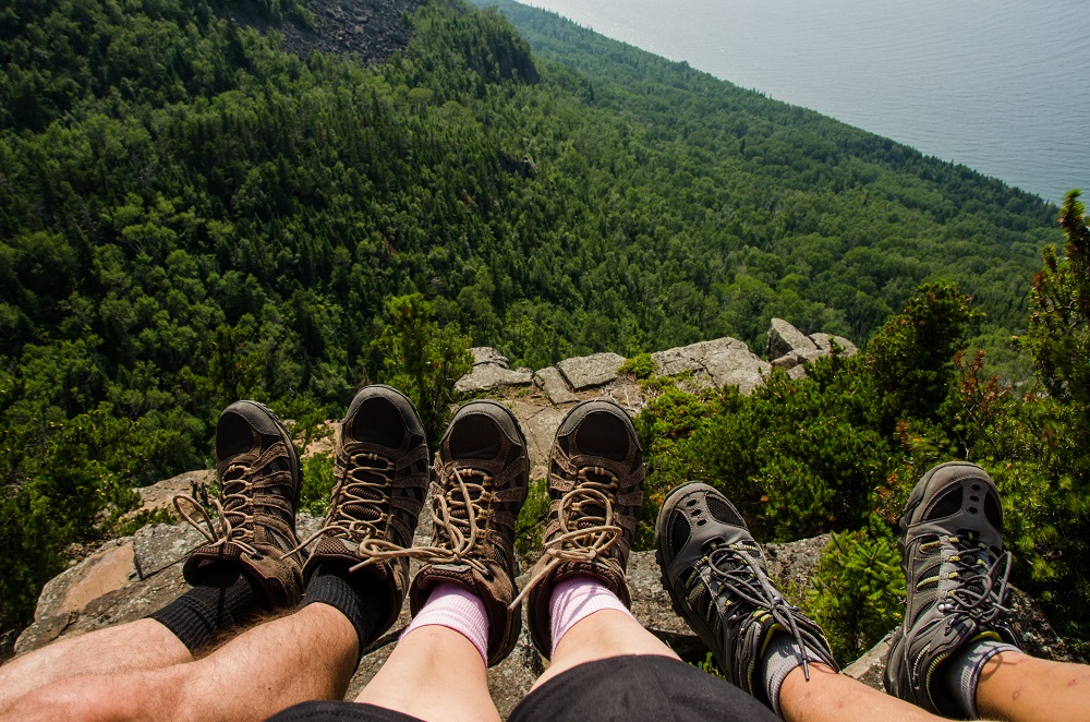 Three people lower legs hanging off the cliff edge wearing hiking boots