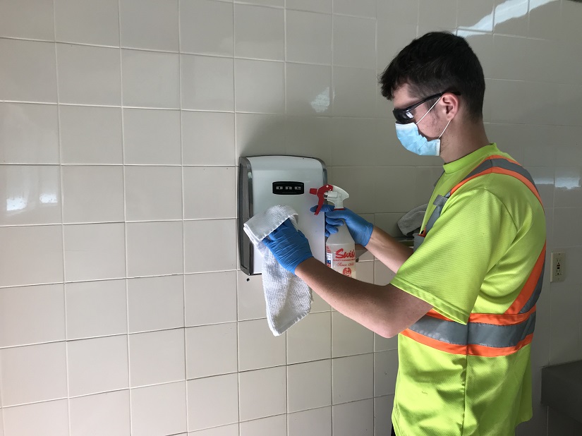 Masked staff member cleaning comfort station.