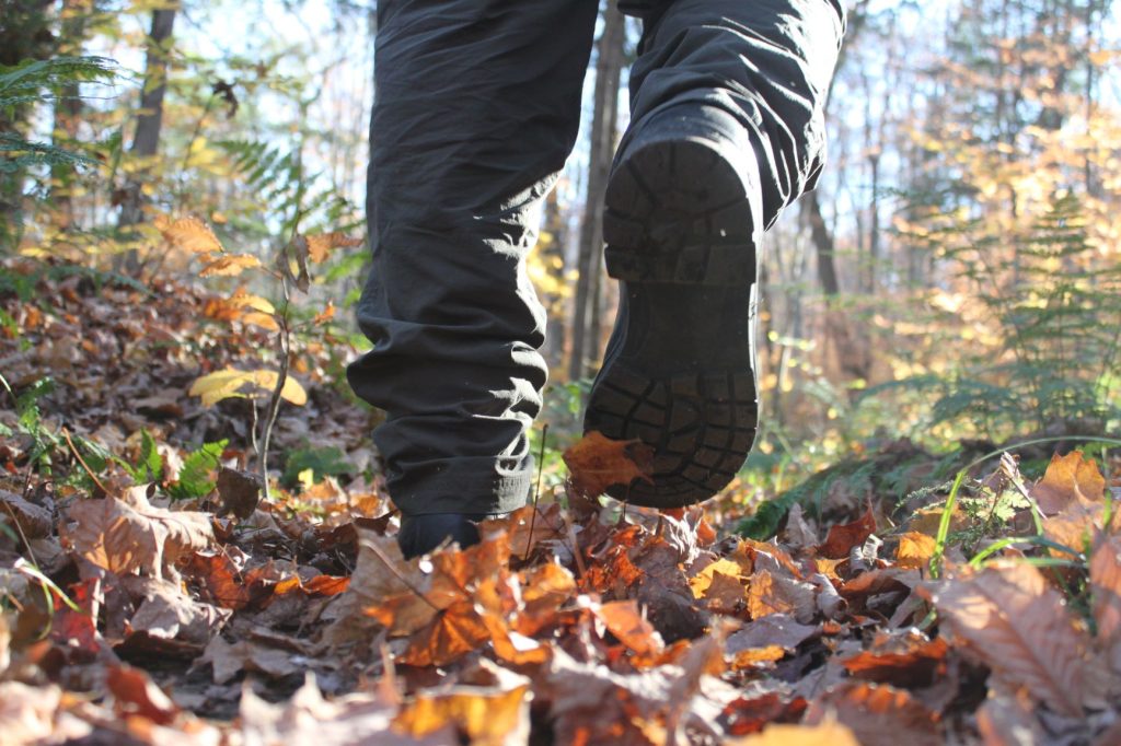 A closeup of someone's hiking boots walking across a leaf-covered trail in the fall