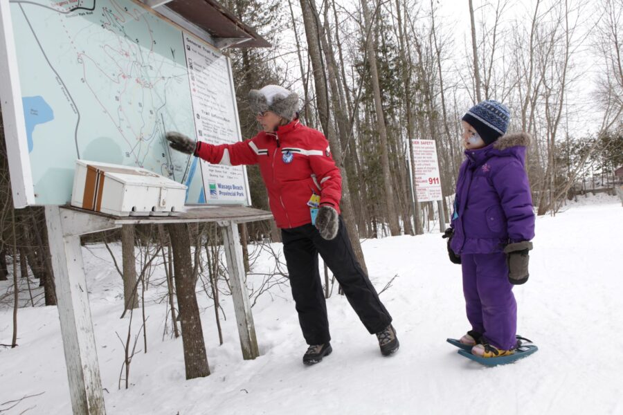 Woman and child wearing snowshoes look at trail map