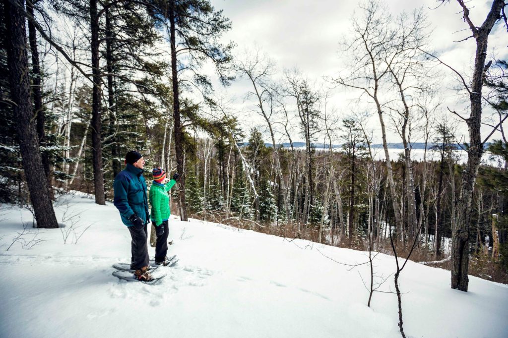 Two people wearing snowshoes standing a snowy lookout in a forest