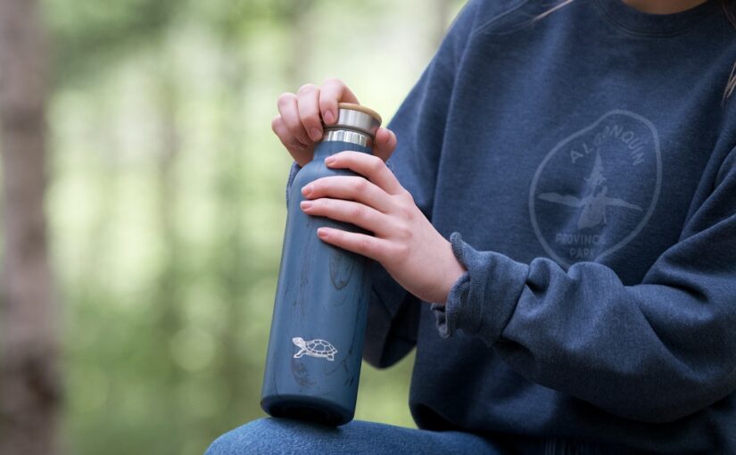 person holding a blue water bottle with a turtle emblem