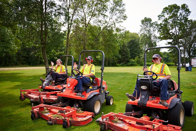 Three park staff waving from lawn mowers.