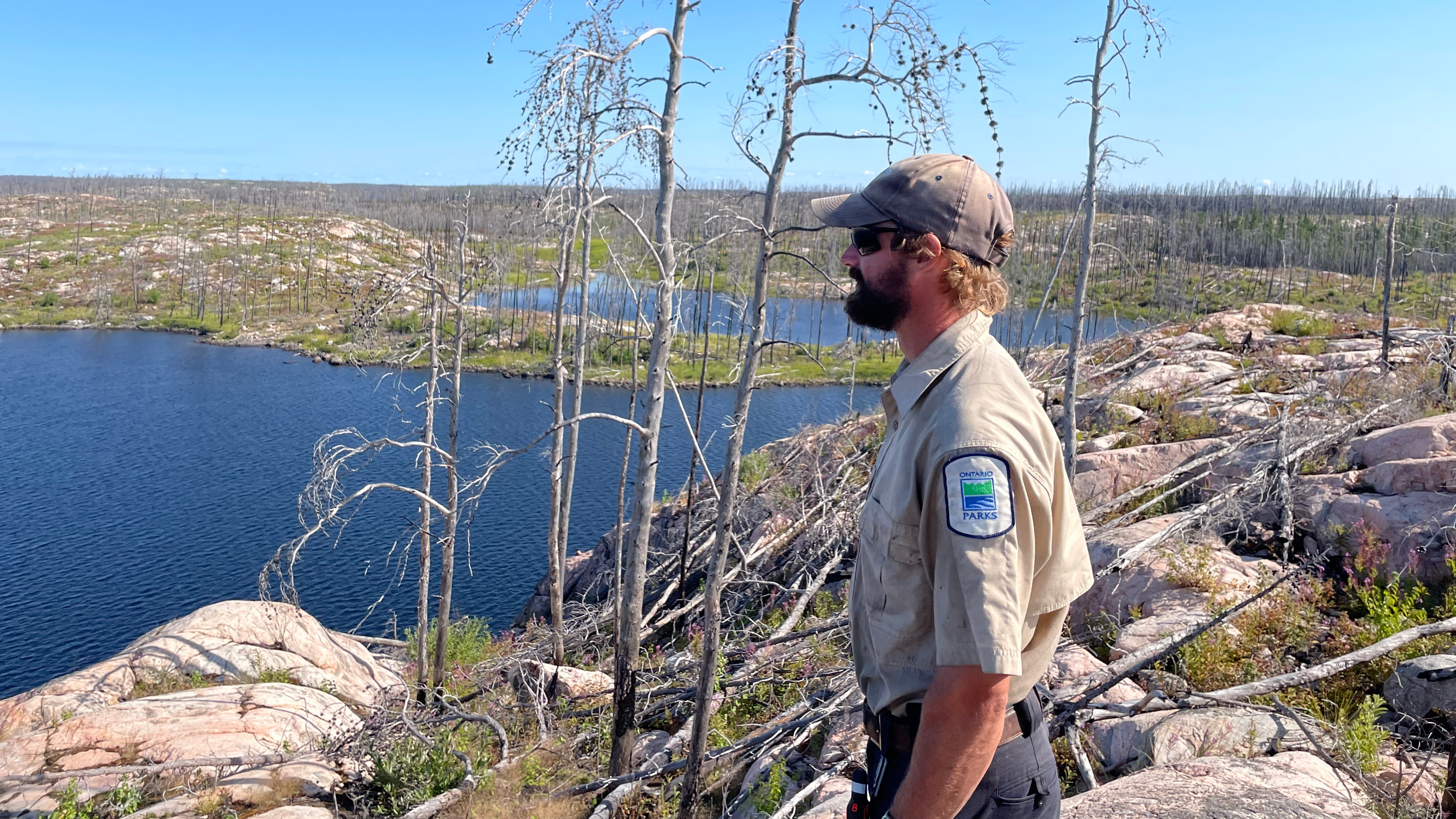 Staff standing on a rocky mountain in the middle of a burn landscape, a lake in the background