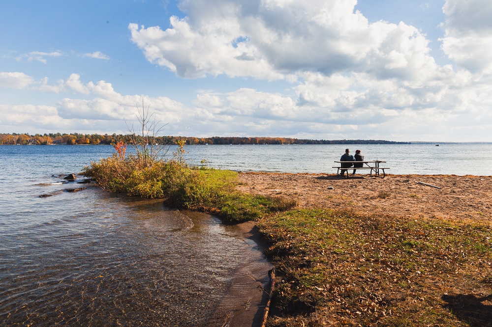 Two people sit at a picnic table on the beach.