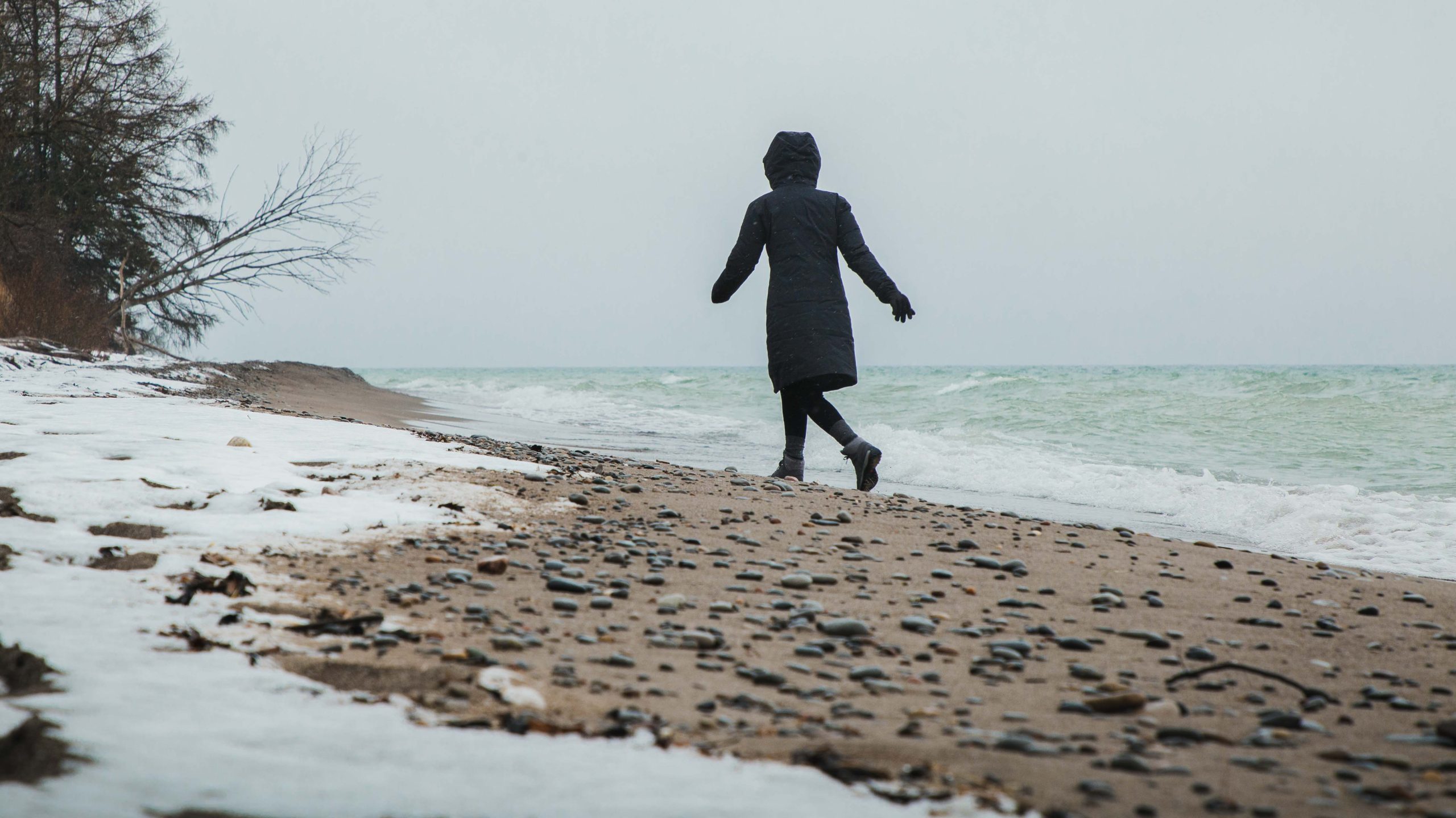 A person walking on a pebbled beach with snow