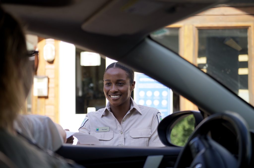 A smiling staff member standing at the open window of a vehicle, giving the driver their permit