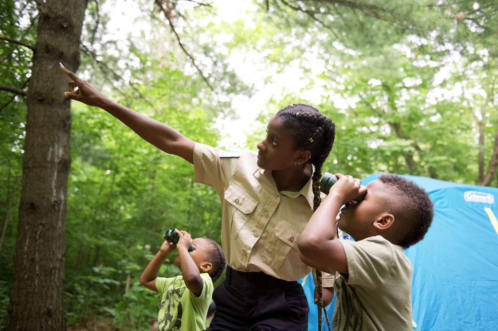 Staff pointing out birds in trees to children with binoculars