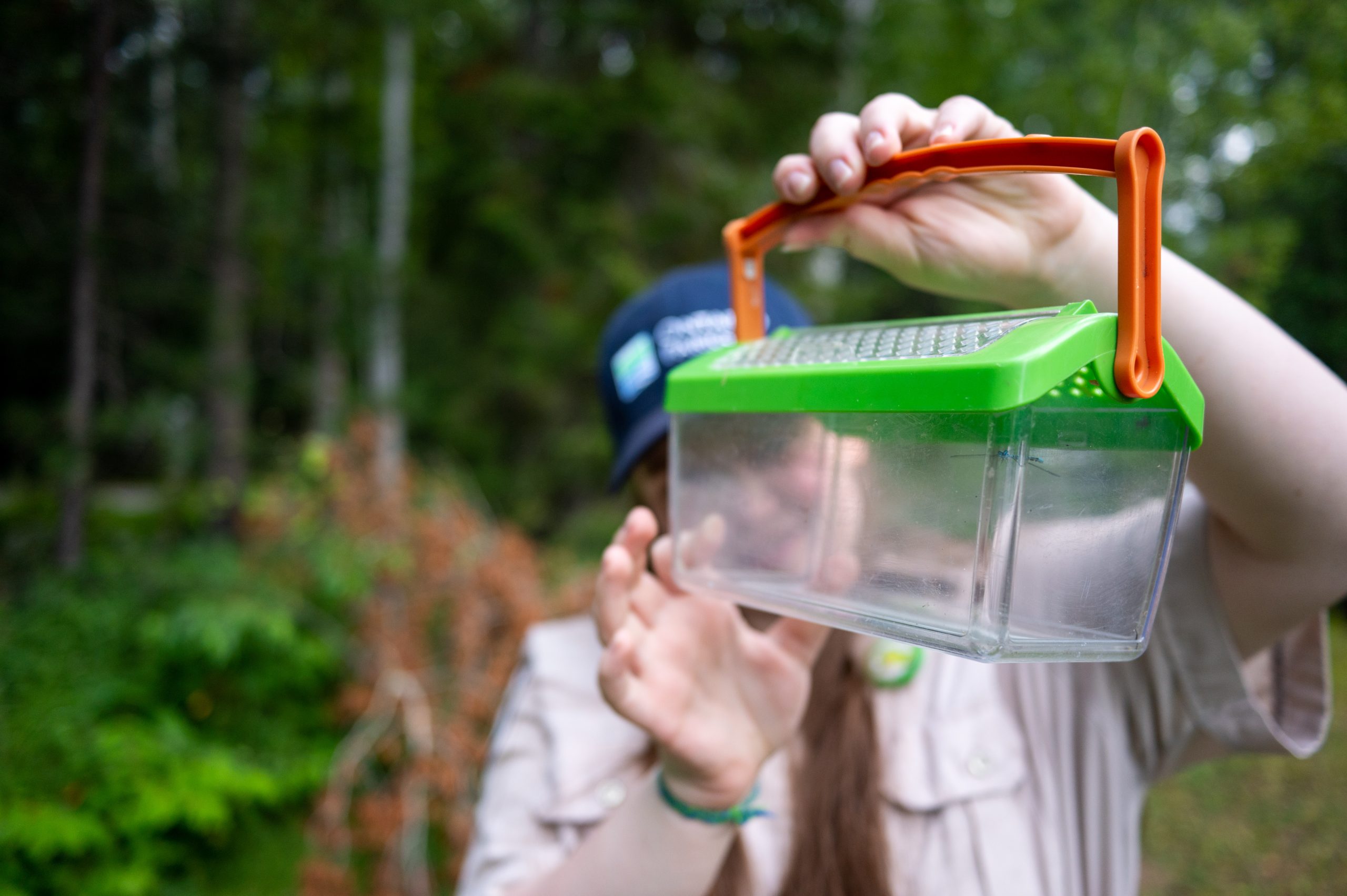 A Discovery Ranger holding a critter container in front of their face to show the camera