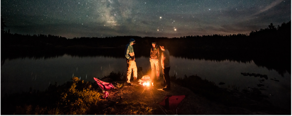 Three people standing around a campfire under a starry sky
