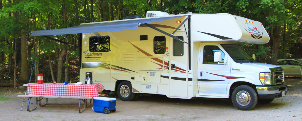An RV on a campsite with a picnic table in front covered with a red tablecloth