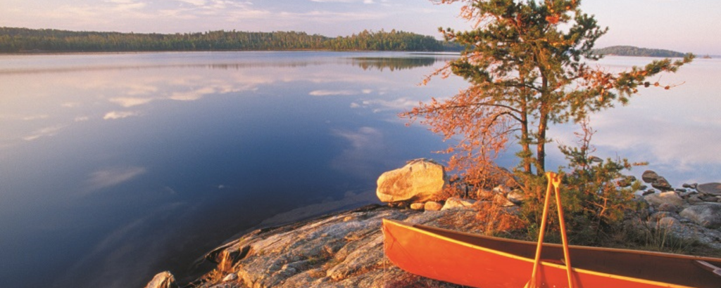 A red canoe and two paddles on a rocky shore of a lake