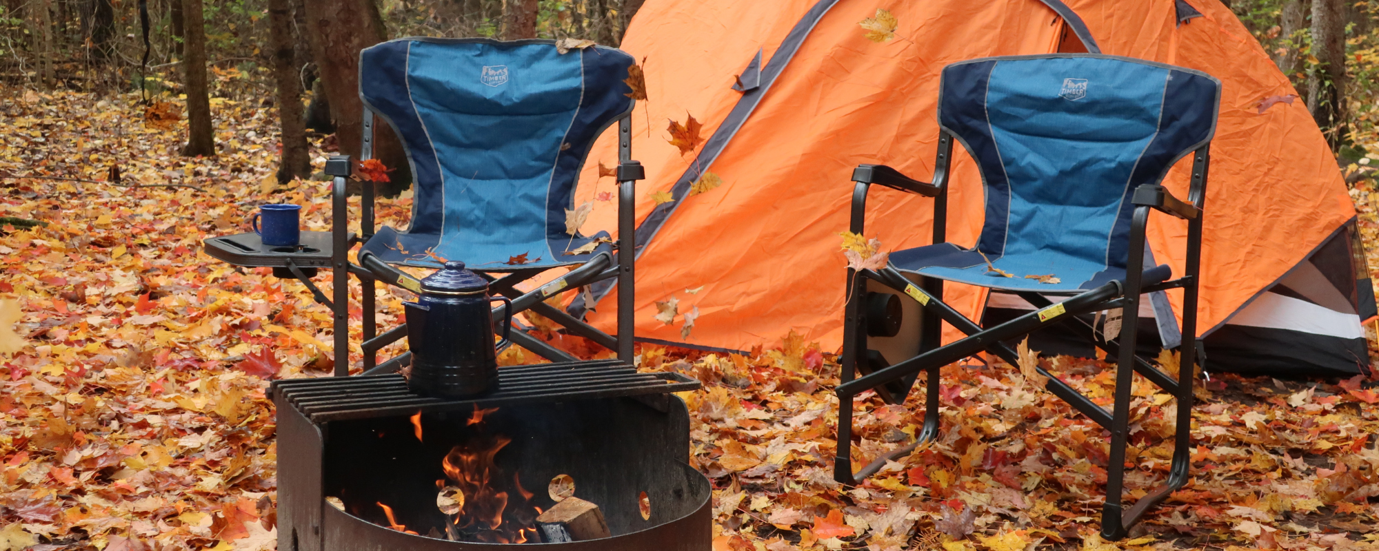 Leaves falling around campfire with 2 camp chairs and 1 tent.