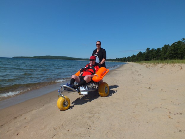 person pushing another in wheelchair on beach