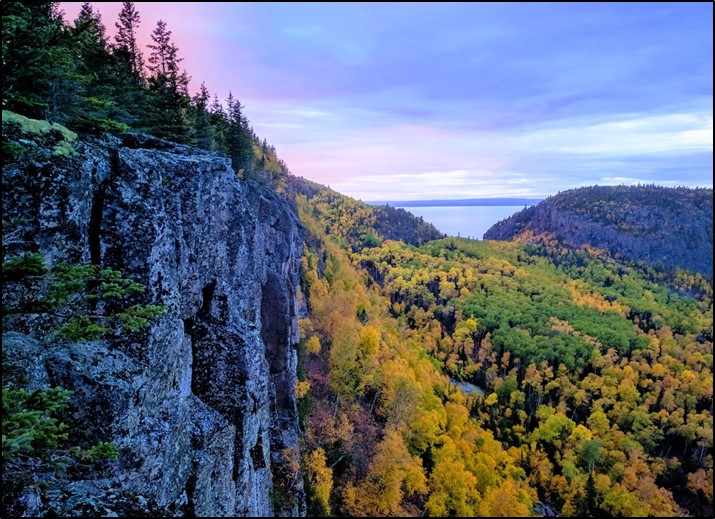 A rock face nest to a forest turning yellow and orange in the fall