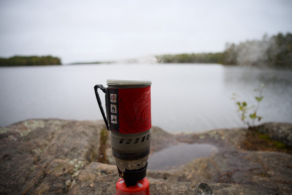 small stove with water boiling on edge of rocky shore