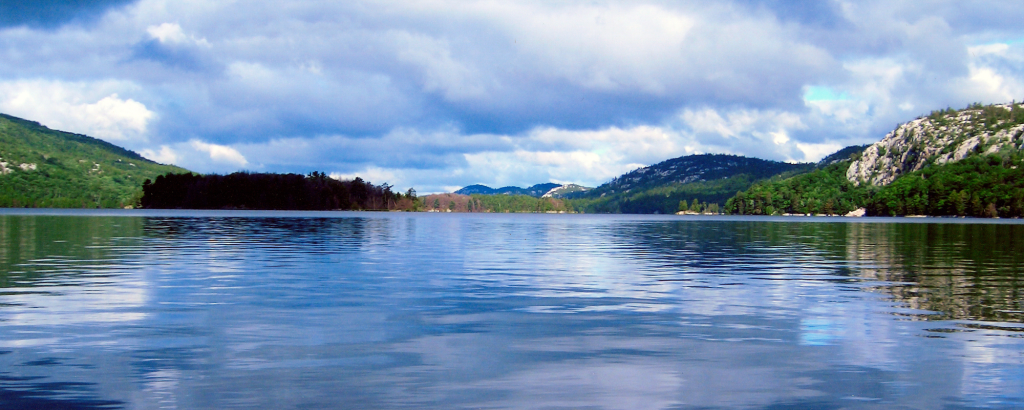 A cloudy sky reflecting on a still lake with forested hills in the background
