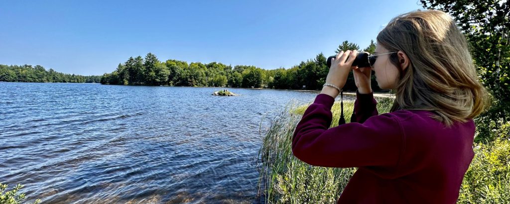 woman looking through binoculars at lake's edge